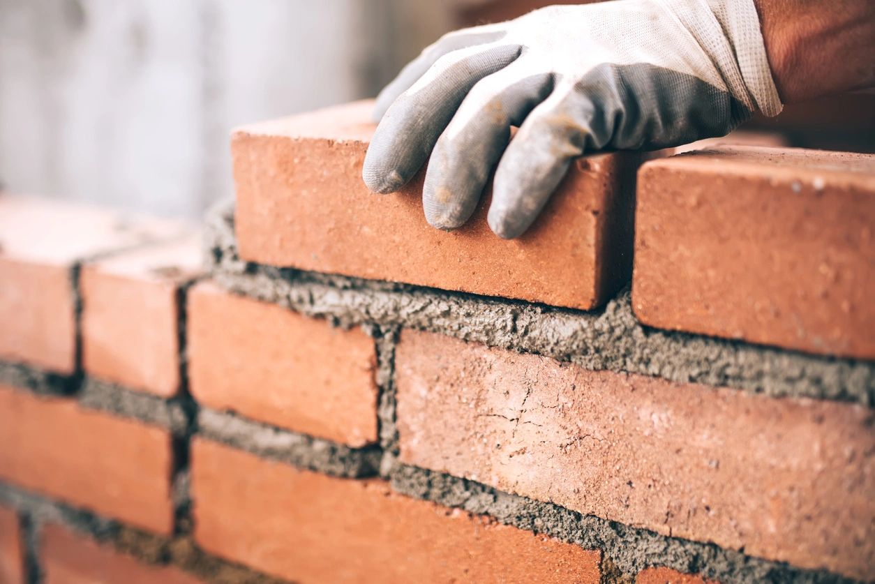 Image of a gloved hand laying bricks.